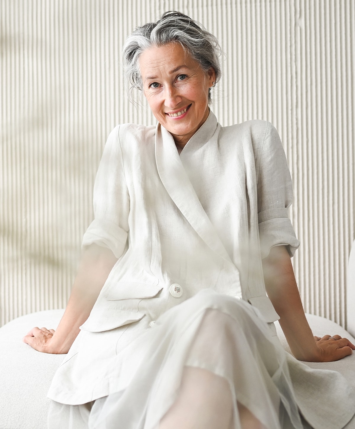 Smiling woman in elegant white outfit, seated.