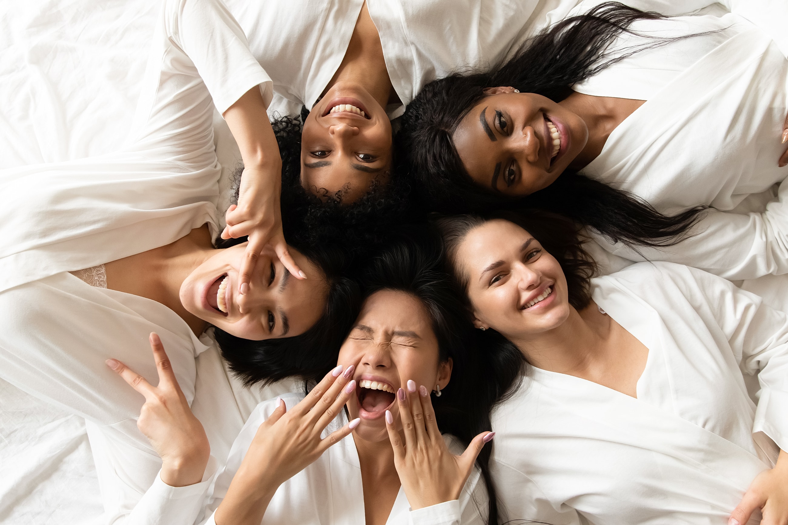 Group of women smiling together on bed.